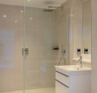 Modern bathroom with a glass shower enclosure, wall-mounted sink, and beige tiled walls and floor.