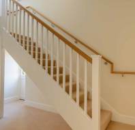 A carpeted staircase with wooden handrails and white balusters in a well-lit interior space.