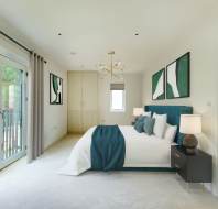 Modern bedroom with a large bed, teal and white bedding, abstract artwork, a chandelier, and glass doors leading to a balcony. Neutral walls and carpet complete the look.