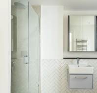 Modern bathroom with a glass shower, herringbone tile, wall-mounted sink, and mirrored cabinet.