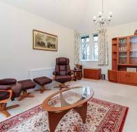 Living room with two brown recliners, a glass coffee table on a red patterned rug, a wooden cabinet with glass doors, and wall art of elephants.