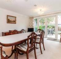 Dining room with a long table and chairs, a painting on the wall, a TV, and a glass door leading to a garden.