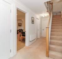 A hallway with cream carpeted floor, a staircase with a handrail on the right, open doors leading to other rooms on the left, and a stairlift attached to the stairs.