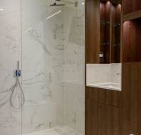Modern bathroom with a glass shower, marble walls, and wooden cabinets.