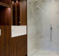 Modern bathroom with a glass shower enclosure, marble walls and flooring, wooden cabinets, and a white toilet.