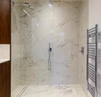 A modern bathroom with a marble-tiled shower, glass door, rainfall showerhead, and a chrome towel rack.