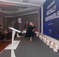 A person walks across the stage at an awards event, with a large screen displaying "Socially Responsible" in the background.