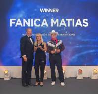 Three people stand on a stage with blue lighting; a woman holds a plaque. The screen reads "Winner Fanica Matias.