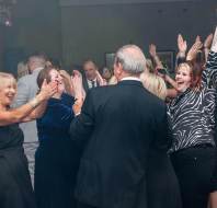 A group of people in formal attire enthusiastically dancing and clapping in a dimly lit room.