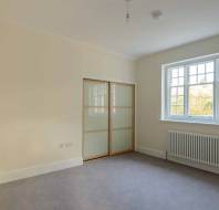 Empty room with beige walls, grey carpet, a window with grid pattern, radiator, and sliding closet doors.