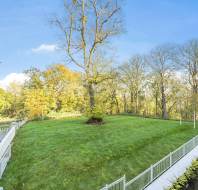 Spacious green lawn with scattered trees, surrounded by a white fence and walkways under a clear blue sky.