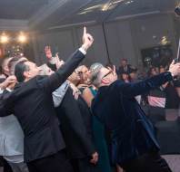 A group of people in formal attire take a selfie together at an indoor event.