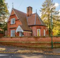 A red-brick Victorian house with a steep roof is surrounded by a brick wall and trees. A sign reading "Abby Lodge, Kew Bridge" is visible in the foreground.