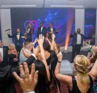 A group of people dancing and enjoying a live band performance during a party in a well-lit event space.