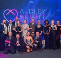 A group of people posing on stage holding awards in front of a sign reading "Audley Spirit Awards.