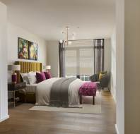 A modern bedroom with a bed, decorative pillows, artwork on the wall, two nightstands with lamps, a chair by the window, and wood flooring. A chandelier hangs from the ceiling.