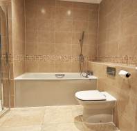 Modern bathroom with beige tiles, featuring a bathtub, shower, wall-mounted toilet, and a sink.