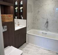 Modern bathroom with marble tiles, a bathtub with a showerhead, a white toilet, a dark wood cabinet with shelves, and a countertop sink.