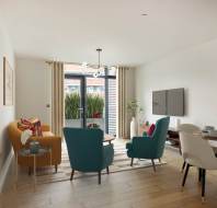 Modern living room with wooden floors, featuring a mustard sofa, two teal chairs, a round dining table, and a flat-screen TV. Large window with curtains opens to a view of greenery.