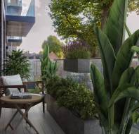 A modern balcony with lush plants, a wooden chair, and a small round table holding a book. A clear glass railing overlooks suburban houses and green trees.