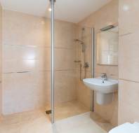 Modern bathroom with beige tiles, a walk-in shower, wall-mounted sink, mirror, towel rack, and a partial view of a toilet.