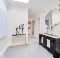 Hallway with a world map on the wall, a table with abstract horse sculptures, a large round mirror, and a black console.
