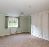 Empty room with light green walls, beige carpet, and a window with curtains. White built-in wardrobe and ceiling light fixture are visible.