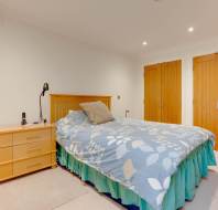 A bedroom with a wooden bed, floral duvet, bedside table, lamp, and two timber closet doors.