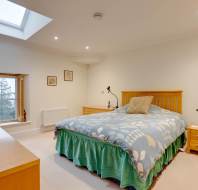 Bedroom with a skylight, bed with floral bedding, wooden headboard, two bedside tables with lamps, and a window overlooking trees.