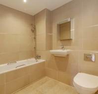Modern bathroom with beige tiled walls and floor, featuring a bathtub, wall-mounted sink, mirror, and toilet.