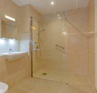 Modern bathroom with a walk-in shower, beige tiled walls, a wall-mounted sink with a mirror above, and a heated towel rail on the right.