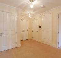 Hallway with cream walls, beige carpet, and several white doors. Three ceiling lights illuminate the space.