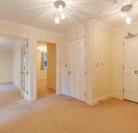 A hallway with beige carpet, white walls, and two ceiling lights. There are doors leading to other rooms and a front door with a mail slot.