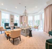 Spacious living room with large windows, chandelier, beige and green seating, and a geometric-patterned rug.