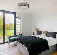Bedroom with a neatly made bed, two lamps on nightstands, a green chair, and a large window showing a view of trees.