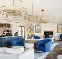Modern lounge area with blue and white furniture, circular chandeliers, art on walls, and a bar with a coffee machine.