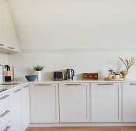 A modern kitchen with white cabinets, a sink, stovetop, and various appliances. A plant and decor items are on the countertop.