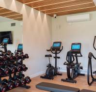 Gym room with dumbbells on racks, a stationary bike, and elliptical machines.装备对面的镜子反射。.