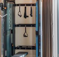 Home gym setup with a bench, cable machine, and various attachments. Beige walls and curtains are visible beside a large window.