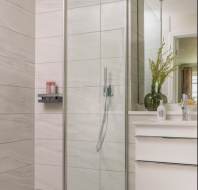 Modern bathroom with glass shower enclosure, gray tiled walls, and a white vanity with a sink and faucet.
