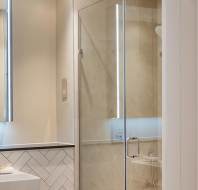 Modern bathroom with a glass shower door, tiled walls, and a lighted mirror above a sink. Creamy beige tones create a warm ambiance.