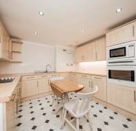 Spacious kitchen with light wood cabinets, black and white tile floor, a small wooden table with two chairs, built-in oven and microwave, and an electric cooktop.