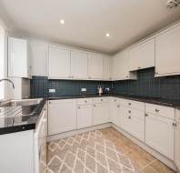 Modern kitchen with white cabinets, dark countertops, and tiled backsplash. Features a built-in oven, sink, and stovetop, with a patterned rug on the tiled floor.