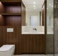 Modern bathroom with a wall-mounted toilet, wooden shelving, a sink with a mirror above, and a glass shower enclosure with gray tiles.