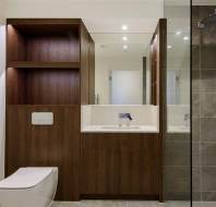 Modern bathroom with a wall-mounted toilet, wooden cabinetry, sink with mirrored cabinet, and a glass-enclosed shower with gray tiles.