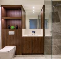 Modern bathroom with a glass-enclosed shower, wooden cabinetry, and a white toilet. A mirror reflects light above a sink with a sleek faucet.