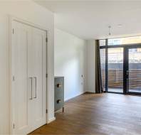 Empty room with wooden floor, a closet on the left, a chest of drawers, and large floor-to-ceiling windows with dark curtains leading to a small patio.