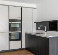 Modern kitchen with sleek grey and black cabinets, built-in oven, stovetop, and a stainless steel sink on a central island. Wood flooring adds warmth to the minimalist design.