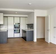 Minimalist modern kitchen with white and gray cabinets, wooden flooring, integrated appliances, and an open door leading to another room.