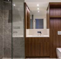 Modern bathroom with glass-enclosed shower, dark wood cabinets, a sink, and a toilet. Walls and floor feature gray tiles.